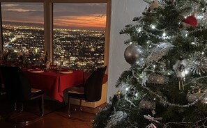 A dining area with a table set for two, overlooking a cityscape at sunset. - Hollywood Hills jetliner views among the stars (Los Angeles)