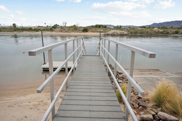 A concrete staircase leading to a dock over a calm river, surrounded by sparse vegetation and distant hills. - RIVERFRONT PARADISE OASIS W/ PRIVATE BEACH & BOAT DOCK (Mohave Valley)