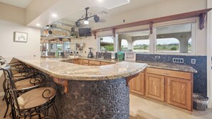 A kitchen with a granite countertop, wooden cabinets, a stone accent wall, and a view of the desert through large windows. - RIVERFRONT PARADISE OASIS W/ PRIVATE BEACH & BOAT DOCK (Mohave Valley)