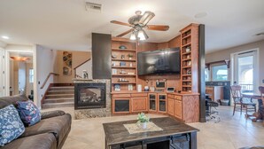 A spacious living area with a fireplace, a large flat-screen TV, wooden shelving, and a dining area with a table and chairs. - RIVERFRONT PARADISE OASIS W/ PRIVATE BEACH & BOAT DOCK (Mohave Valley)