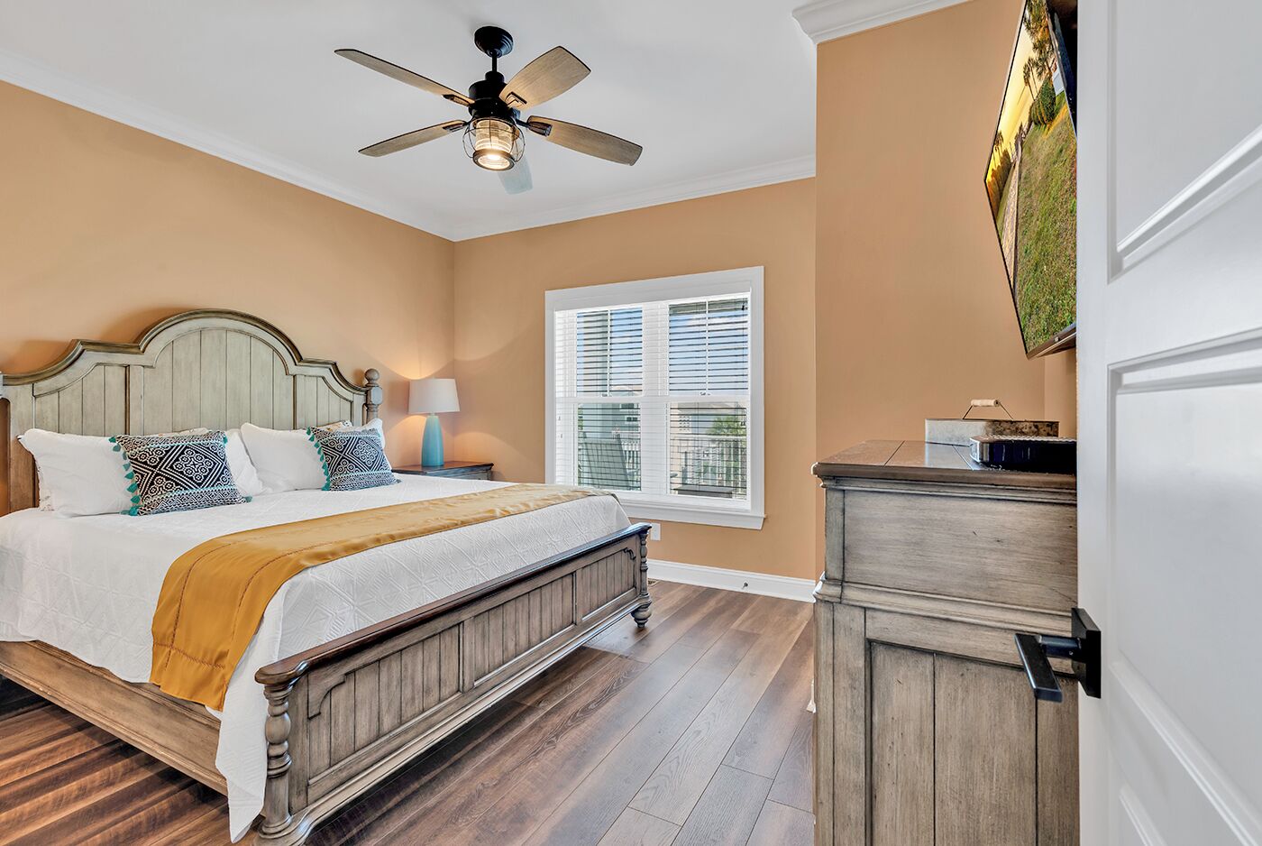 A bedroom with a bed, a nightstand, a dresser, a ceiling fan, and a window with blinds.
