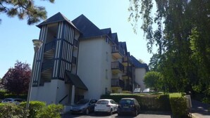 Un immeuble résidentiel à plusieurs étages, doté d’un escalier central, de balcons et d’un espace de stationnement avec des voitures.