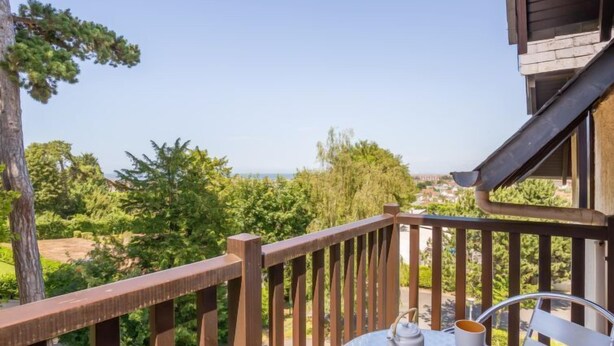 Un balcon avec une table et des chaises, offrant une vue sur un paysage luxuriant et un panorama lointain.
