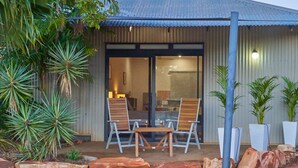 A building with a corrugated metal exterior, a glass door entrance, and two wooden tables with chairs outside. - Quiet Studio Hideaway 5 minutes Walk to Cable Beach (Cable Beach)