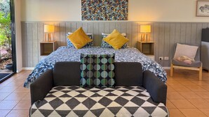 A bedroom with a bed, two bedside lamps, a sofa, a patterned throw, and a view of greenery outside. - Quiet Studio Hideaway 5 minutes Walk to Cable Beach (Cable Beach)