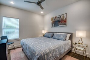 A bedroom with a bed, a desk, a chair, a ceiling fan, a window with blinds, and a wall-mounted painting. - Relax in this Hillside Home with Canyon Lake Views (Canyon Lake)
