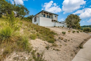 A modern two-story house with a flat roof, located on a hillside with sparse vegetation. - Relax in this Hillside Home with Canyon Lake Views (Canyon Lake)