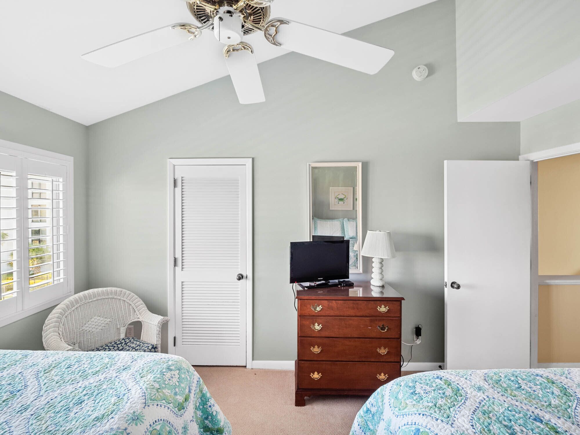 Une chambre avec deux lits, un ventilateur de plafond, une commode, un téléviseur et une fenêtre avec des stores.