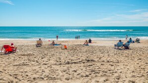 A beach with people sunbathing and swimming, and a clear blue sky.