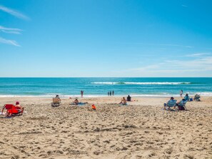 A beach with people sunbathing and swimming, and a clear blue sky.