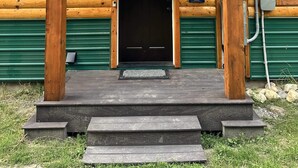 Eine Blockhütte mit grünem Metalldach, einer Holzterrasse und einer schwarzen Tür.