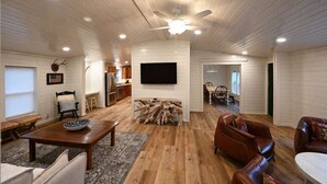 Ein geräumiges Wohnzimmer mit Holzboden, einem Wand-Fernseher und einer Essecke mit Tisch und Stühlen.