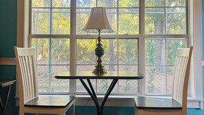 A room with a table and two chairs, a lamp, and a large arched window with a view of trees. - Amazing Studio, 5 minutes to the Private Beach.  (Myrtle Beach)