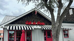 A cafe with a red awning and black and white striped awnings, outdoor seating with wicker chairs and a table, and a tree in the foreground. - Amazing Studio, 5 minutes to the Private Beach.  (Myrtle Beach)