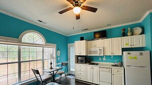 A kitchen with white cabinets, a microwave, and a refrigerator. There is a window with a view of trees and a ceiling fan. - Amazing Studio, 5 minutes to the Private Beach.  (Myrtle Beach)