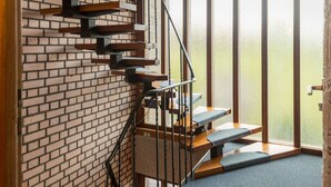 A modern staircase with wooden steps and metal railings, leading to a room with a brick wall and large windows. - Eifelnatur (Haus 1) by Interhome (Immerath)