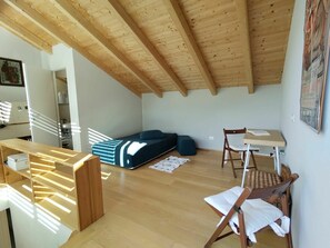 Quarto estilo loft com teto de madeira, um sofá, uma mesa pequena e uma cadeira.