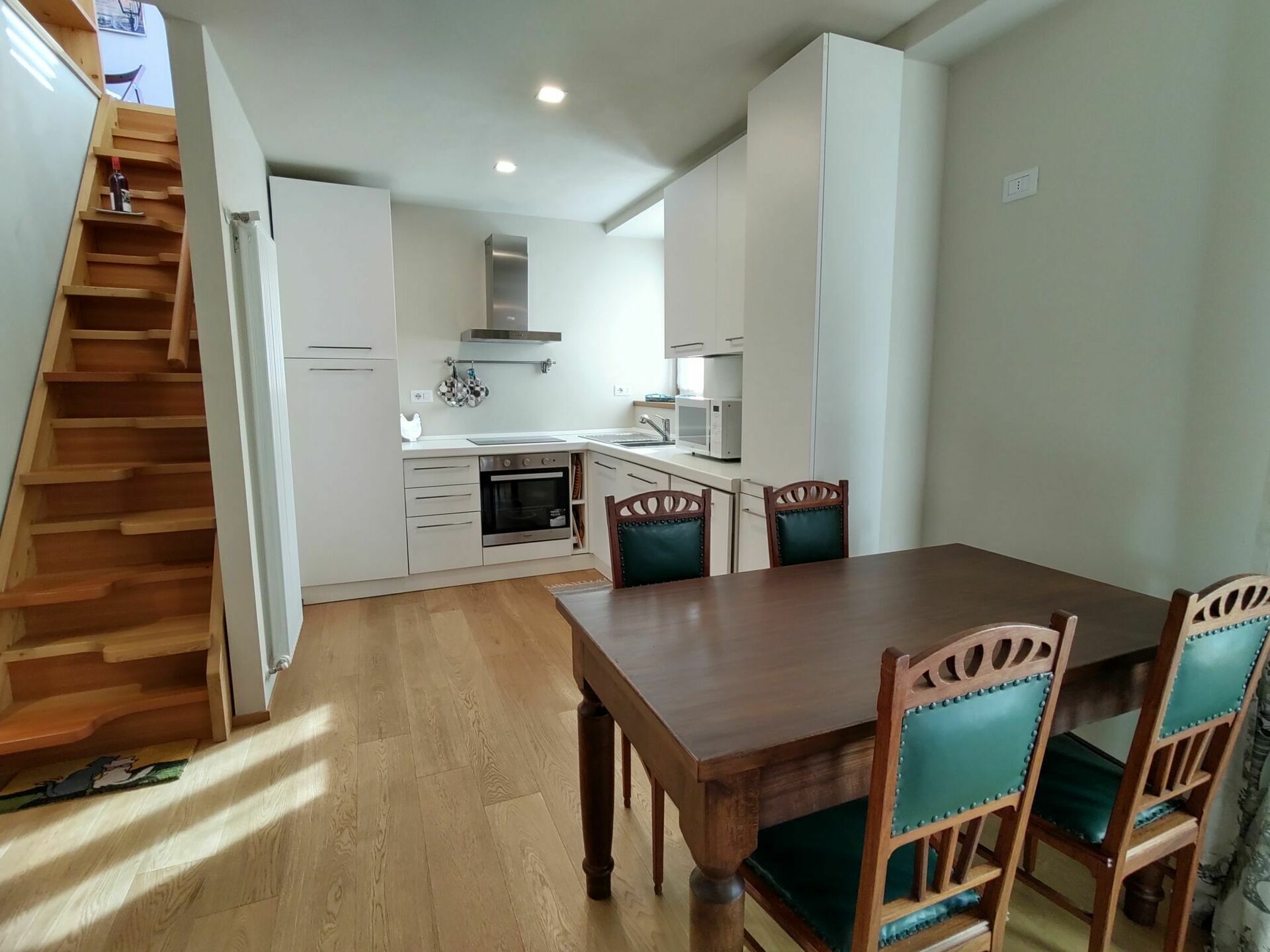 Una cocina compacta con alacenas blancas, microondas y estufa. Hay una mesa de comedor de madera con sillas.