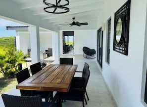A modern dining area with a wooden table and black chairs, a ceiling fan, and a view of the outdoors.