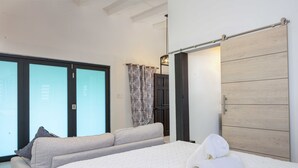 A bedroom with a bed, a sofa, a wardrobe, and a sliding glass door leading to a balcony. - Carthys Estate (Saint philip)