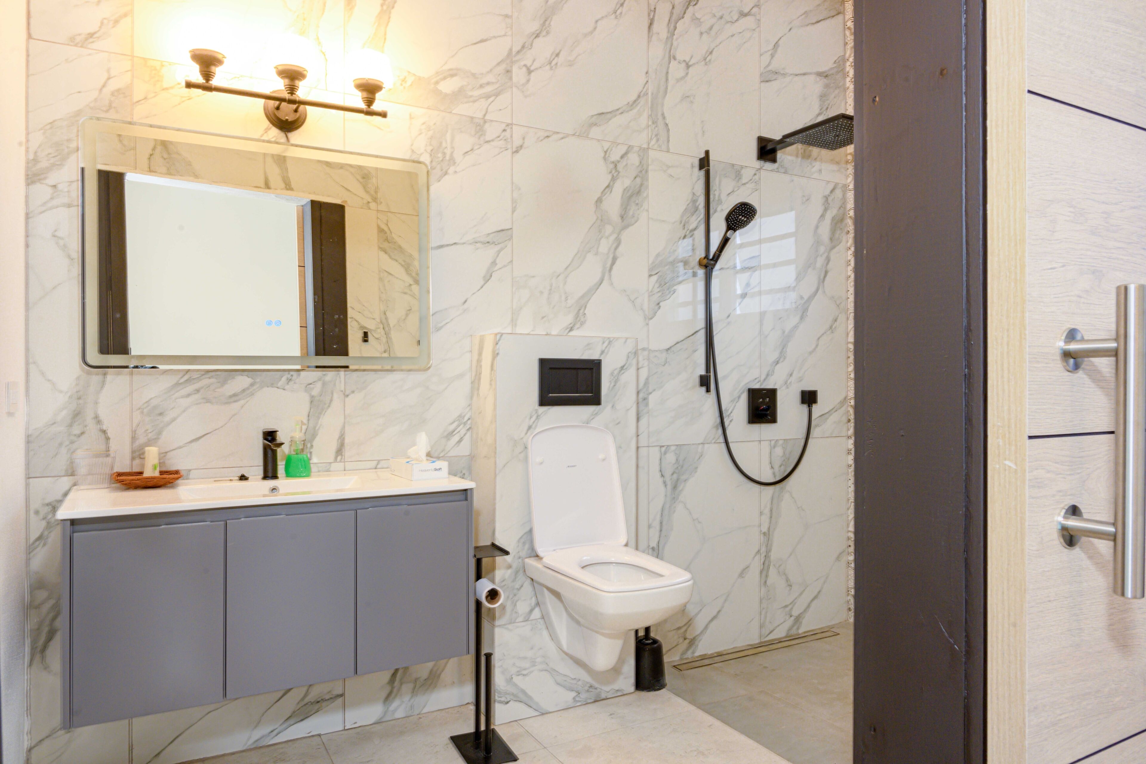 Un baño con pared de mármol, un lavabo con espejo, un inodoro y una ducha.