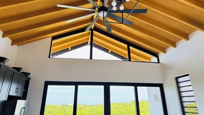 A room with a sloped wooden ceiling, a ceiling fan, and large windows offering a view of greenery. - Carthys Estate (Saint philip)