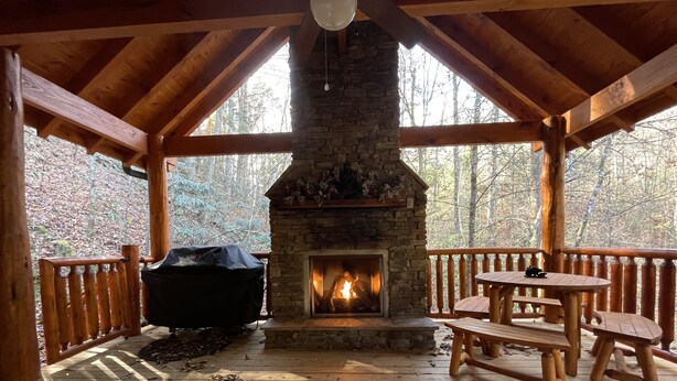 A covered wooden deck with a stone fireplace, outdoor seating, and a grill. - Papa Bear’s Retreat, Cedar Falls, 2 BD, 3 BA, Queen Bunk Bed in loft, Fireplaces (Sevierville)