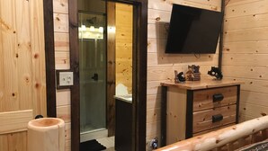 A wooden-paneled bathroom with a glass shower enclosure, a mounted TV, and a wooden vanity with drawers. - Papa Bear’s Retreat, Cedar Falls, 2 BD, 3 BA, Queen Bunk Bed in loft, Fireplaces (Sevierville)