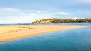 A beach with clear blue water, sandy shore, and a rocky hill in the background.