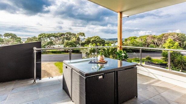 A balcony with a glass-top table, two wine glasses, and a vase with flowers.
