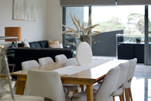 Een moderne eethoek met een houten tafel, witte stoelen en een vaas met gedroogde planten.
