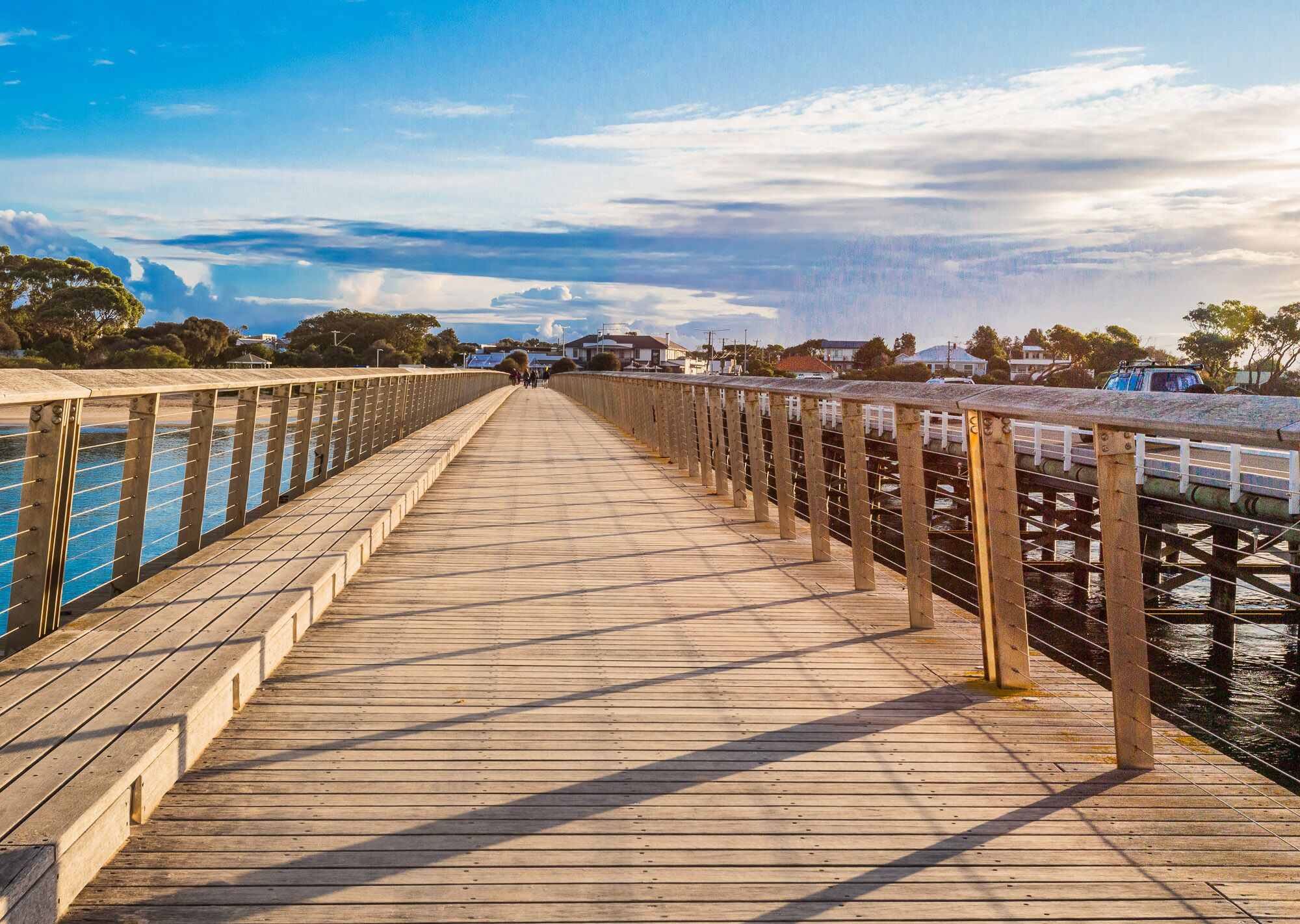 A wooden boardwalk with railings, leading to a body of water.