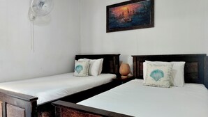 A room with two wooden beds, each with a white mattress and decorative pillows, a white wall-mounted fan, and a framed painting above the beds. - The Azure - M'Pai Bay (Koh Rong Sanloem)