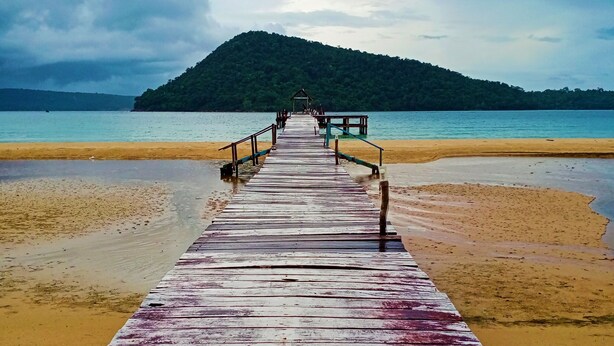 A wooden pier leading to a beach with a mountain in the background. - The Azure - M'Pai Bay (Koh Rong Sanloem)