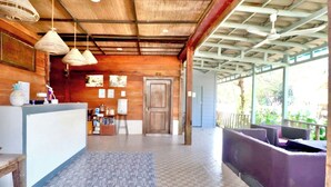 A reception area with a checkered floor, wooden walls, and a wooden door. There are hanging lights, a reception desk, and a seating area with purple cushions. - The Azure - M'Pai Bay (Koh Rong Sanloem)