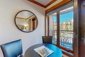 Enjoy a room with a round table and two chairs, a large mirror, and a window offering a view of the balcony and surrounding buildings.