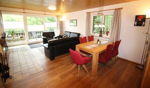 A living room with a sofa, red chairs, a wooden dining table, and a balcony with a view. - Fewo Schwarzwald 1060m - Ferienwohnung (Todtnauberg)