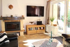 Ein Wohnzimmer mit Kamin, Fernseher, Bücherregal und Blick ins Freie.