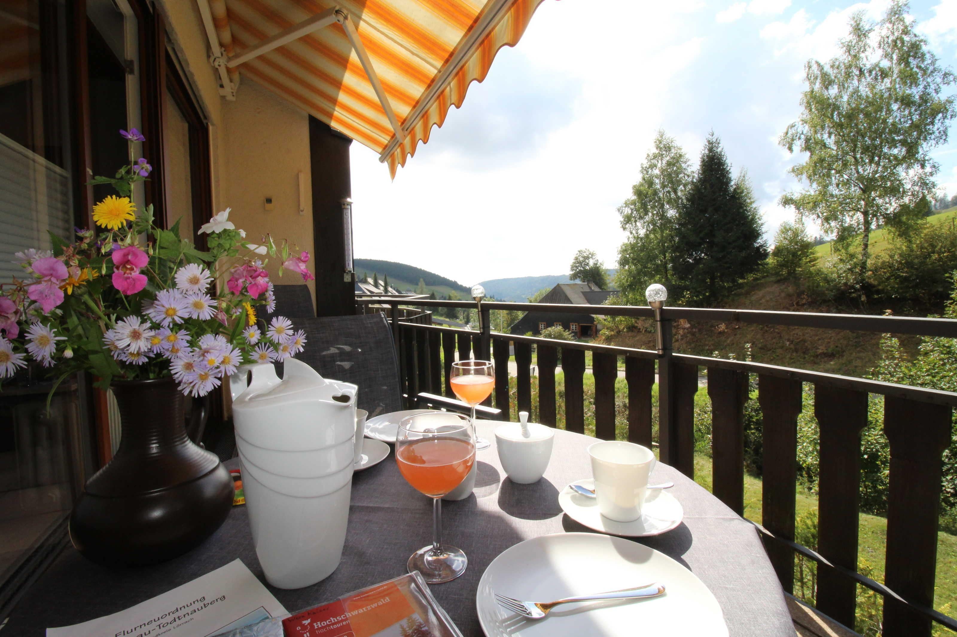 Ein Tisch im Freien mit Blick auf Hügel, eine Blumenvase und ein Getränk.