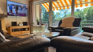 Ett vardagsrum med lädersoffor, ett soffbord, en tv som är monterad på väggen och ett stort fönster med en orange markis.