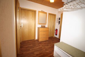 Une pièce avec un plancher en bois, une armoire en bois, un miroir au-dessus d’une commode et un extincteur fixé au mur.