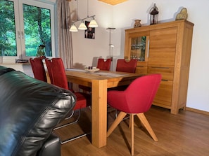 Un comedor con mesa de madera, sillas rojas, un armario y ventana con vistas a árboles.