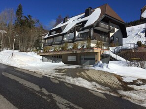 Un immeuble à plusieurs étages doté de balcons, d’un garage et surplombant un paysage enneigé.
