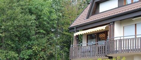 A two-story building with a balcony, surrounded by dense trees.
