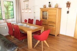 Ein Essbereich mit einem Holztisch, roten Stühlen, einem Schrank mit Glastüren und einem Fenster mit Blick auf Bäume.
