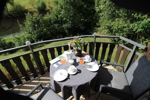 Une table installée à l’extérieur, offrant une vue sur la verdure, avec une terrasse en bois et une chaise.