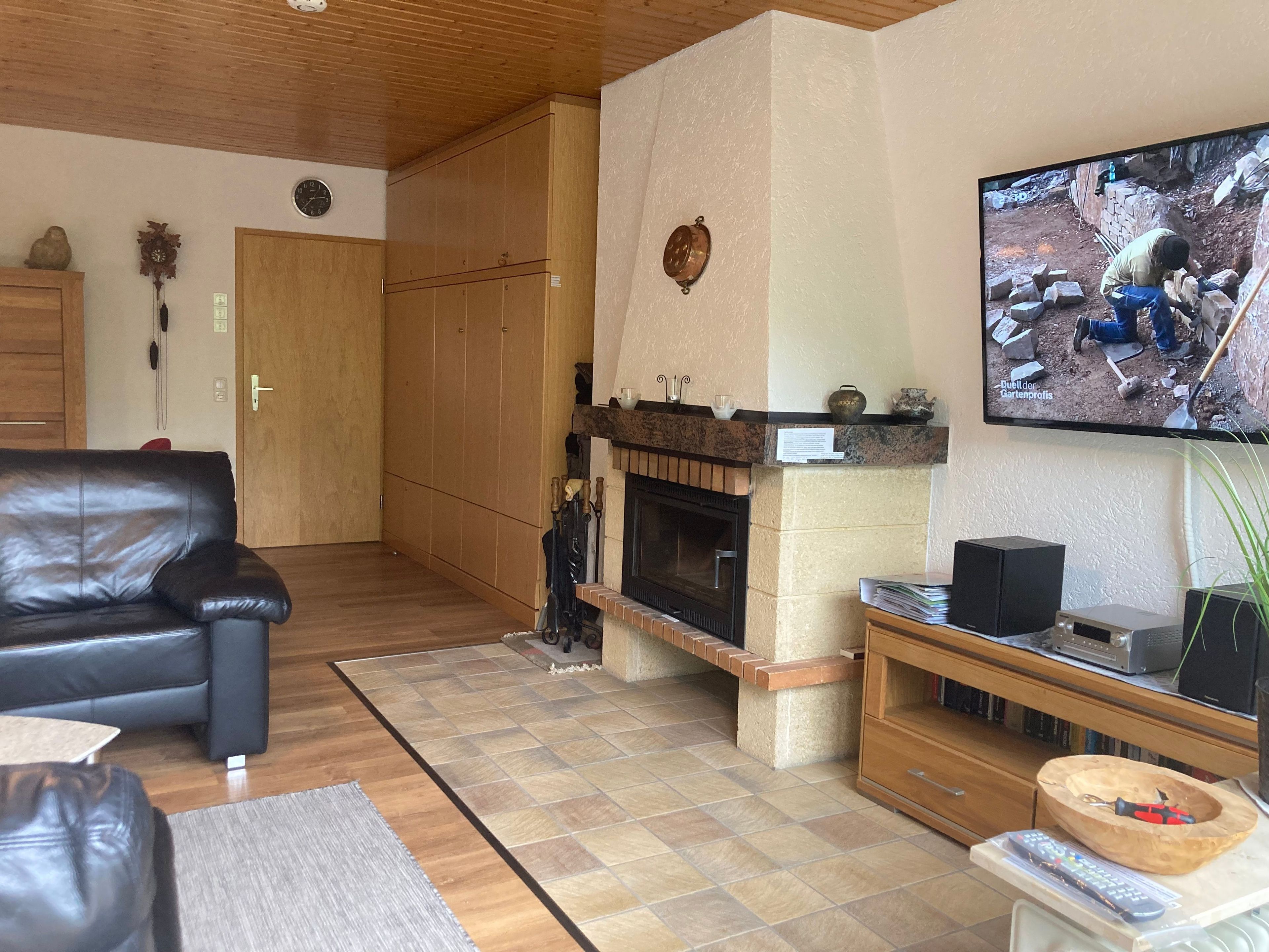 Un salon avec une cheminée, un téléviseur fixé au mur, un canapé en cuir et un meuble en bois.