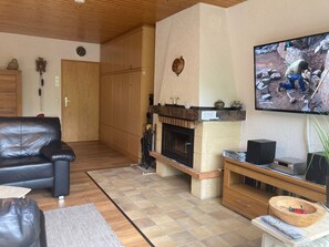 A living room with a fireplace, a television mounted on the wall, a leather sofa, and a wooden cabinet. - Fewo Schwarzwald 1060m - Ferienwohnung (Todtnauberg)