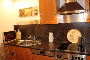 A kitchen with a stainless steel sink, a stove, wooden cabinets, and a coffee-themed wall decoration. - Fewo Schwarzwald 1060m - Ferienwohnung (Todtnauberg)