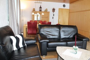 A living room with a sofa, a dining table with chairs, a clock on the wall, and a wooden cabinet. - Fewo Schwarzwald 1060m - Ferienwohnung (Todtnauberg)